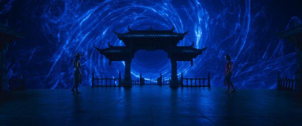 A dramatic scene from Mortal Kombat II featuring two characters facing each other on a dark stone platform, with an ornate traditional Chinese-style structure in the background and a swirling blue energy vortex behind them.