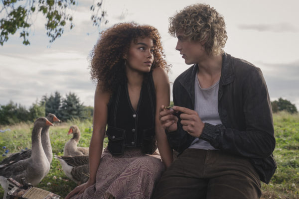 Still from The Hunger Games: Sunrise on the Reaping featuring Whitney Peak as Lenore Dove Baird and Joseph Zada as Haymitch Abernathy, seated together on the grass with geese nearby, conveying a moment of connection.