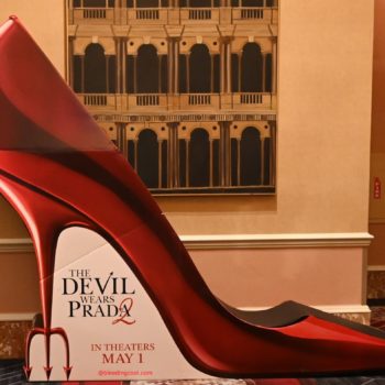 A large, eye-catching show standee in the shape of a bright red stiletto heel, promoting 'The Devil Wears Prada 2' with the release date of May 1 displayed at the base.