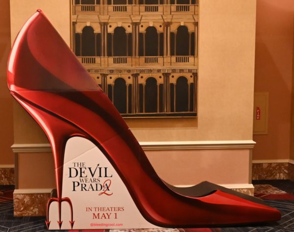 A large, eye-catching show standee in the shape of a bright red stiletto heel, promoting 'The Devil Wears Prada 2' with the release date of May 1 displayed at the base.