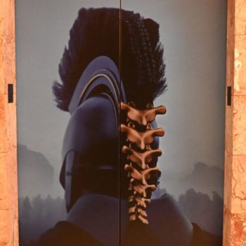 A promotional poster for the film 'The Odyssey' features a stylized representation of a character in a dark helmet with a mohawk, and a prominent spine design. The release date, July 17, 2026, is displayed at the bottom.
