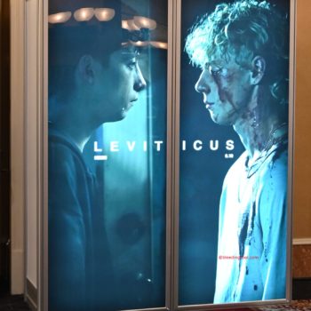A promotional display for the film 'Leviticus' at CinemaCon 2026 features two characters in profile, one appearing distressed and injured, while the other looks contemplative. The title 'LEVI TICUS' is boldly featured prominently between the two figures.