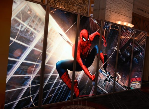 A vibrant promotional display featuring Spider-Man, depicted in a dynamic pose as he swings between skyscrapers. The background showcases a cityscape, emphasizing the action and excitement around the 'Spider-Man: Brand New Day' event.