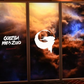 A promotional display featuring the title 'Godzilla Minus Zero' in bold white lettering against a dramatic background of colorful clouds. The display also includes a stylized 'G' logo and the release date '11.06.2026'.