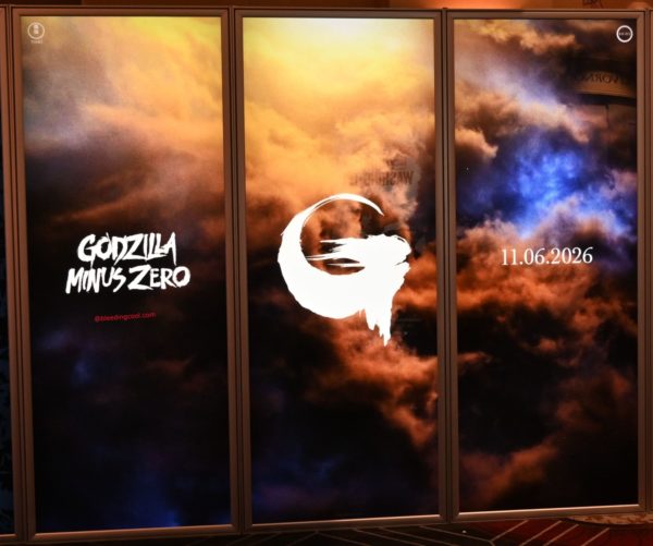 A promotional display featuring the title 'Godzilla Minus Zero' in bold white lettering against a dramatic background of colorful clouds. The display also includes a stylized 'G' logo and the release date '11.06.2026'.