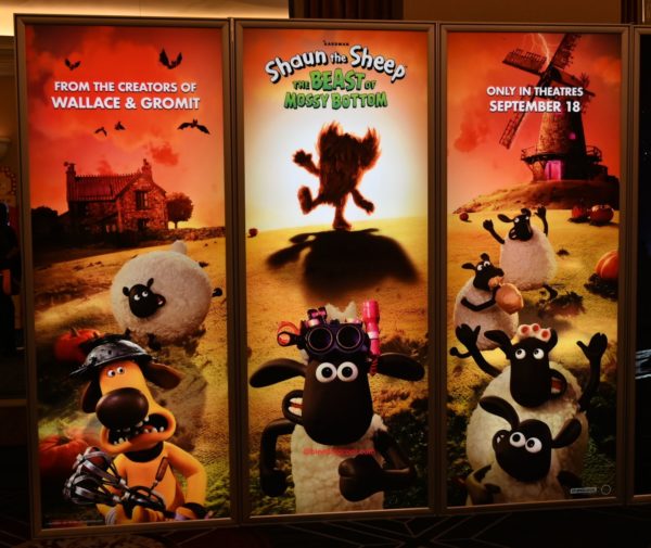 A promotional display for the movie 'Shaun the Sheep: The Beast of Mossy Bottom' featuring characters from the film, including a sheep and a dog with exaggerated expressions, set against a vibrant, colorful background. The display highlights the movie's release date of September 18 and mentions its creators, Wallace & Gromit.