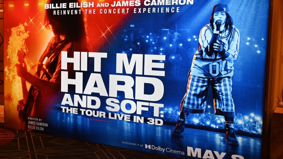 A promotional display for the concert experience 'Hit Me Hard and Soft' featuring Billie Eilish and James Cameron, with vibrant graphics and the event date May 8 prominently featured.