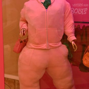 NEON - A fashion display featuring a mannequin dressed in an oversized pink hoodie and matching pants, showcased against a vibrant pink background. The mannequin has a gold-colored head and chunky accessories, representing a playful streetwear aesthetic.