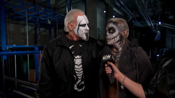 Darby Allin, whose face is painted like a skull, interacts closely with Sting, who has white face paint and a black attire, both in a backstage area at AEW Dynamite. An interviewer holds a microphone toward them.