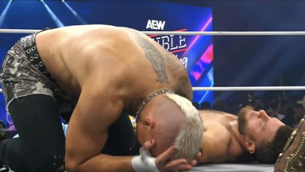In a wrestling ring, a visibly upset Darby Allin kneels, holding his head while MJF lies on the mat beside him, signifying the aftermath of a match. The AEW logo and vibrant lights are visible in the background.