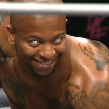 Lio Rush, a professional wrestler, displays an intense expression during a match, showcasing his tattoos and unique personality. The lighting highlights his determined look.