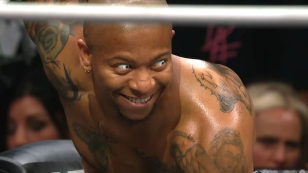 Lio Rush, a professional wrestler, displays an intense expression during a match, showcasing his tattoos and unique personality. The lighting highlights his determined look.