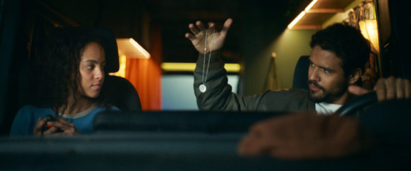 Passenger - A scene from the movie 'Passenger' featuring Lou Llobell as Maddie and Jacob Scipio as Tyler, inside a vehicle. Tyler is holding a necklace while both characters engage in conversation.