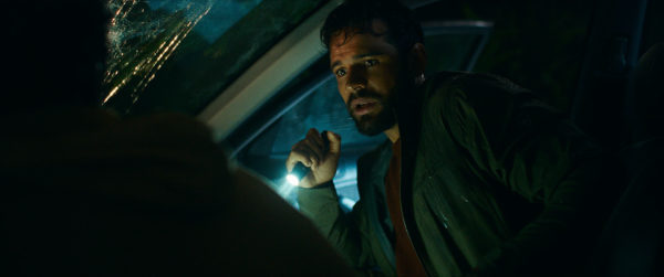 Passenger - A still from the movie 'Passenger' featuring Jacob Scipio as Tyler, sitting inside a car with a concerned expression, holding a flashlight. The scene is dimly lit, emphasizing a tense atmosphere.