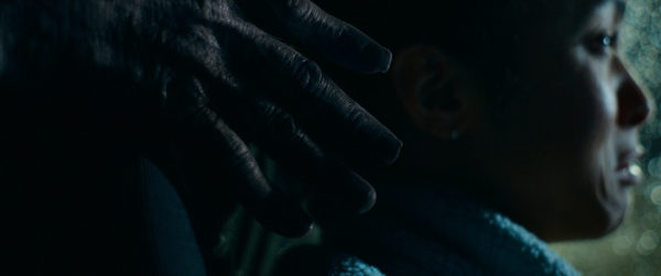 Passenger - A scene from the film 'Passenger' features a close-up of a young woman, Maddie, looking distressed as a dark, menacing hand reaches towards her. The background is blurred with lights, adding a tense atmosphere.