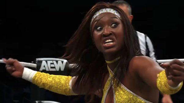 A professional wrestler, dressed in a sparkling yellow costume, passionately gestures and displays a fierce expression in the AEW Dynamite wrestling ring.