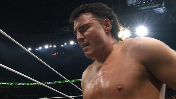 Speedball Mike Bailey looks conflicted in the wrestling ring after his partner Kevin Knight captures the TNT Championship. Bright lights and a dark arena set the scene for this emotional moment.