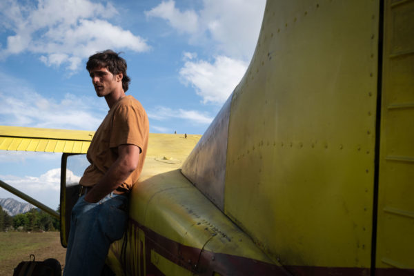 Jacob Elordi portrays Hig leaning against a yellow aircraft under a blue sky with scattered clouds in a scene from 20th Century Studios' 'The Dog Stars.'