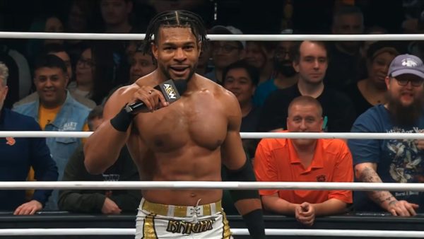 TNT Champion Kevin Knight stands in the wrestling ring, holding a microphone and speaking to an engaged crowd. He has a muscular build and wears distinctive wrestling attire.