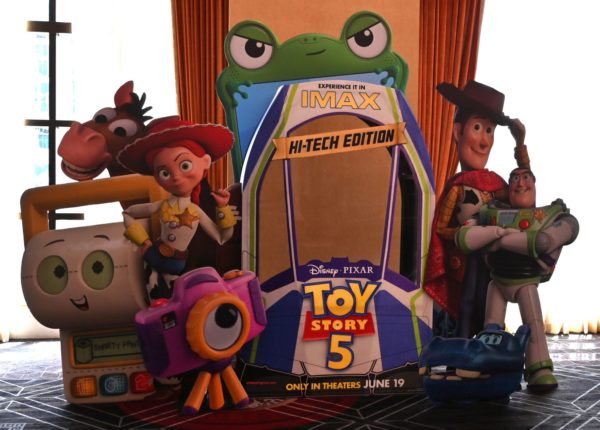 A colorful display featuring characters from Toy Story 5, including Woody, Buzz Lightyear, Jessie, and others, alongside an IMAX standee promoting the film's release on June 19. The standees are set against a backdrop of curtains, creating a playful and vibrant atmosphere.