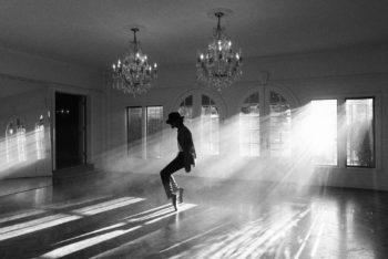 Jaafar Jackson portraying Michael Jackson in a black-and-white scene, dancing in a softly lit room with chandeliers and beams of light creating a dramatic atmosphere.