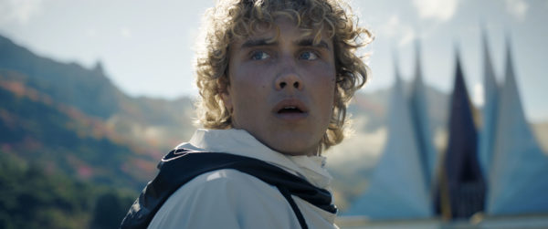 A still from 'The Hunger Games: Sunrise on the Reaping' featuring Joseph Zada as Haymitch Abernathy, gazing thoughtfully with a concerned expression, surrounded by scenic mountains and a brightly lit sky.